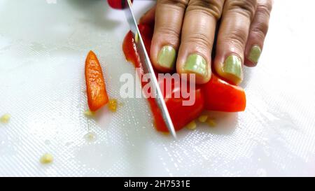 Ein Slicing süßen roten Pfeffer auf Schneidebrett. Weibliche Hand schneidet Paprika mit Messer. Blick von oben Stockfoto