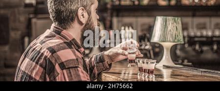 Trinken von Alkohol in Schnapsgläser in einem Nachtclub oder einer Bar. Bärtiger Mann Schüsse Cocktail. Tequila Shots, Wodka, Whisky, Rum. Barkeeper im Pub. Tequila-Schuss Stockfoto