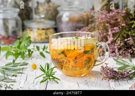 Auf dem Tisch eine Tasse gesunden Calendula Kräutertee, Heidekraut, Rosmarin, Kamille und Salvia Heilkräuter und Blumen. Gläser getrockneter Heilkräuter Stockfoto