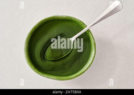 Grünes Chlorella-Algenpulver in einer Schüssel mit einem Löffel auf hellem Hintergrund Stockfoto