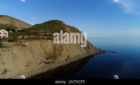 Atemberaubende Luftaufnahme des offenen Meeres und einer kleinen grünen Insel. Aufnahme. Atemberaubende grüne Gras bedeckte Klippe mit einsamen Häusern in der Nähe ruhigen blauen Meer wate Stockfoto