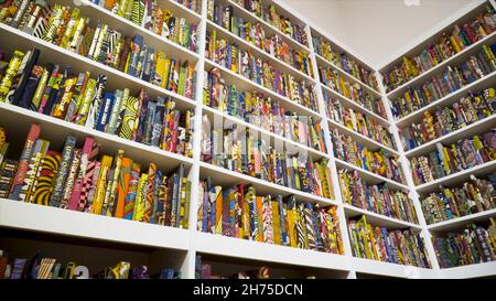 Bücherregal mit vielen bunten Büchern in Mustern. Aktion. Bücher mit bunt gemusterten Einbänden werden stilvoll in großen Regalen abgelegt. Stockfoto