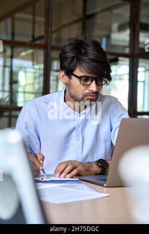 Ein junger indischer Geschäftsmann schaut sich das Webinar im Büro auf einem Laptop an. Stockfoto