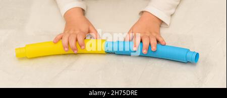 Anonymes Kind mit bunten Pop-Rohr Spielzeug Spiel. Nahaufnahme eines Banners mit Kinderhände, die mit einem Spielzeug aus Pop-Tubes spielen. Stockfoto