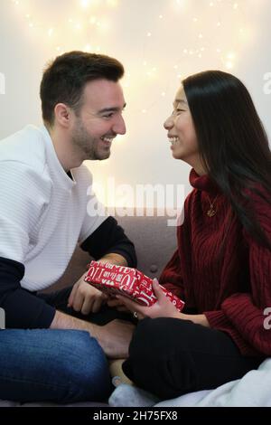 Junge, multiethnische, glückliche Paare tauschen Weihnachtsgeschenke aus. Stockfoto