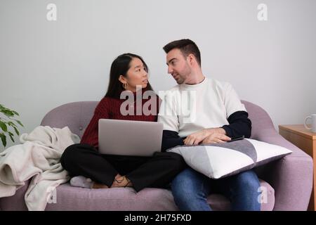 Junges Paar, das sich zu Hause mit einem Laptop auf der Couch entspannt und spricht. Stockfoto