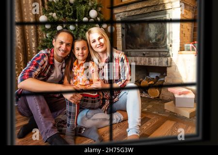 Große Familie mit drei Kindern feiert Weihnachten zu Hause. Festliches Abendessen am Kamin und Weihnachtsbaum. Eltern und Kinder essen am Kamin in Stockfoto