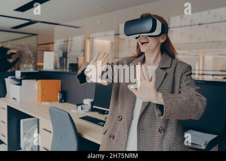 Frau mit VR-Headset, die im Büro im Virtual Reality-Spiel Spaß hat Stockfoto
