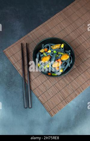 Nudeln schwarz mit Gemüse und Muscheln servieren, asiatische Lebensmittel mit Essstäbchen Stockfoto