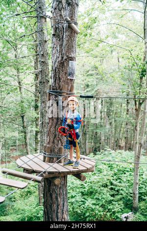 Boy in Schutzkleidung steht auf einer hölzernen Plattform vor der Agility Bridge Stockfoto