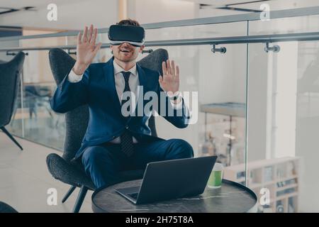 Geschäftsmann in formellem Anzug und in VR-Headset-Brillen, die auf wıth offene Handflächen in der Luft zeigen Stockfoto