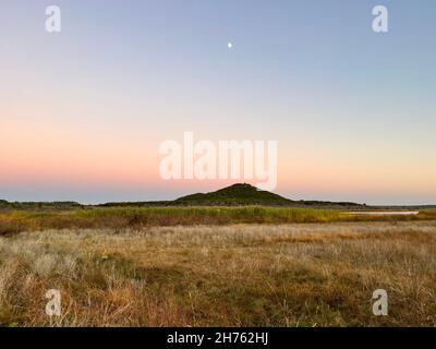 Der zauberhafte, farbenfrohe Dämmerungshimmel während der Mond über dem Horizont der Bergspitze aufsteigt, weht die frische kühle Brise über die grasbewachsene Tundra in Texas. Stockfoto