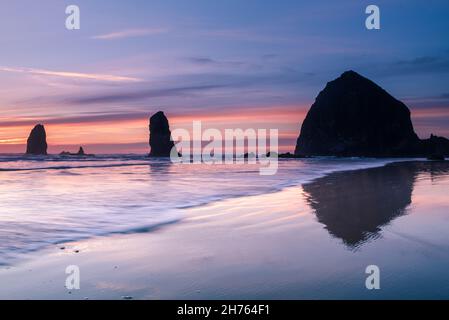 Wellen vor dem Cannon Beach Heuhaufen bei Sonnenuntergang Stockfoto