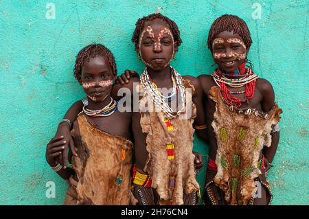 Drei junge Mädchen aus dem Stamm Hamar mit bemalten Gesichtern, Perlen und Tierhäuten, die typisch für ihren Stamm sind Stockfoto