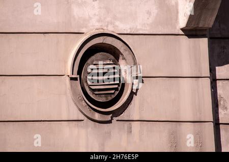 Altes ovales Kreisfenster auf Steinfassade mit rostigen Metallschaft Stockfoto