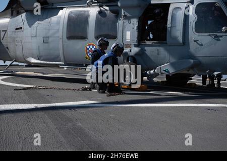 211119-N-TC847-1403 OSTCHINESISCHES MEER (NOV 19, 2021) Seeleute entfernen Choke und Ketten zu einem MH-60s Seahawk, der dem Hubschrauber-Seekampfgeschwader (HSC 4) zugewiesen ist. Higgins wird Commander, Task Force (CTF) 71/Destroyer Squadron (DESRON) 15, der größten vorwärtseingesetzten DESRON der Marine und der wichtigsten Surface Force der US-Flotte von 7th, zugewiesen. (USA Navy Foto von Mass Communication Specialist 3rd Class Christine Montgomery/veröffentlicht) Stockfoto