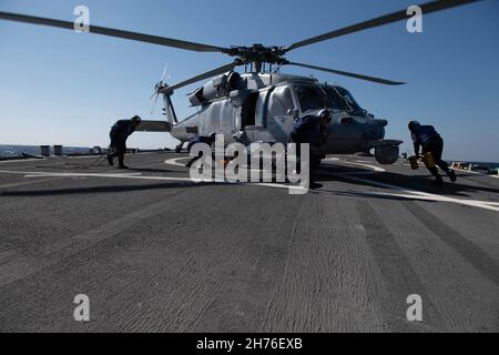 211119-N-TC847-1356 OSTCHINESISCHES MEER (NOV 19, 2021) Matrosen ersticken und ketten einen MH-60s Seahawk, der dem Hubschrauber-Seekampfgeschwader (HSC 4) zugewiesen wurde. Higgins wird Commander, Task Force (CTF) 71/Destroyer Squadron (DESRON) 15, der größten vorwärtseingesetzten DESRON der Marine und der wichtigsten Surface Force der US-Flotte von 7th, zugewiesen. (USA Navy Foto von Mass Communication Specialist 3rd Class Christine Montgomery/veröffentlicht) Stockfoto