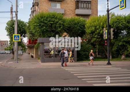 Ein Kiosk mit einem Schild Einzelhandel Druck, in russischer Sprache, steht auf dem Bürgersteig in der Nähe eines Fußgängerübergangs mit Menschen an einem Sommertag. Stockfoto