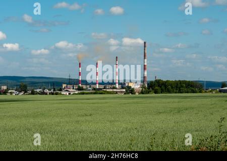 Nazarovskaya GRES mit rauchenden Kaminen im Sommer, hinter einem Weizenfeld gesehen, befindet sich in der Stadt Nazarovo, Region Krasnojarsk, Russland. Stockfoto