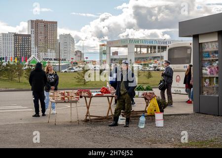 Ein Mann steht an einer Bushaltestelle vor der Kulisse eines Einkaufszentrums im Frühjahr in der Nähe einer hausgemachten Theke mit Gemüse und Obst. Stockfoto