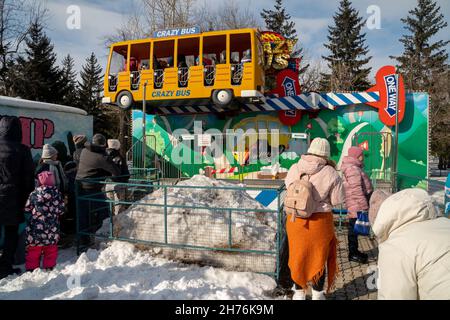 Im Frühling stehen die Menschen vor der Kulisse der Bäume im zentralen Stadtpark vor der Attraktion Crazy Bus. Stockfoto