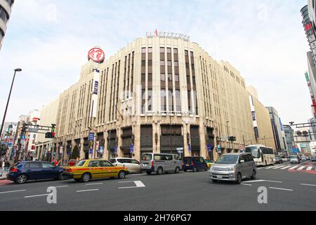 Der Isetan Shinjuku Flagship-Store in Shinjuku, Tokio, Japan, mit Taxis und anderen Fahrzeugen, die an einer belebten Kreuzung vorbeifahren. Stockfoto