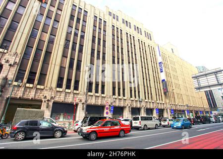 Der Isetan Shinjuku Flagship-Store in Shinjuku, Tokio, Japan, mit Taxis und anderen Fahrzeugen, die an einer belebten Kreuzung vorbeifahren. Stockfoto