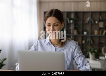Frau, die an einem Laptop arbeitet, sitzt im modernen Homeoffice-Zimmer Stockfoto
