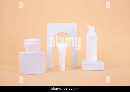 Set aus White Cream Tube Mockup auf weißem Podium mit Bogen auf beigem Hintergrund. Natural Beauty Creme Kosmetik Make-up Produkt. Verpackung oder Branding-Präsentation Stockfoto