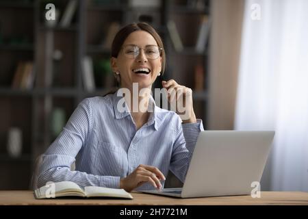 Eine glückliche Geschäftsfrau sitzt am Schreibtisch vor dem Laptop Stockfoto