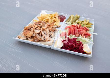 Döner, türkischer Chicken Döner Servierplatte auf weißem Teller neben Salat, Gurken und Pommes auf dem Tisch Stockfoto