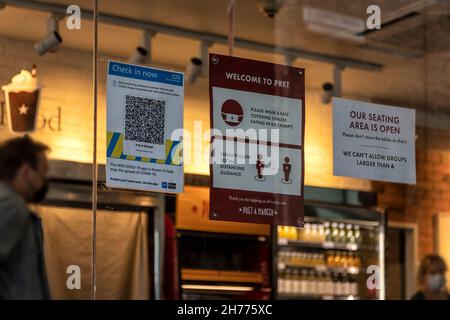 LONDON, Großbritannien - 14. JULI 2021: Covid-19 Soziale Distanzierungshilfe an einem Schaufenster einer Krippe mit unfokussierten Menschen, die Masken tragen Stockfoto