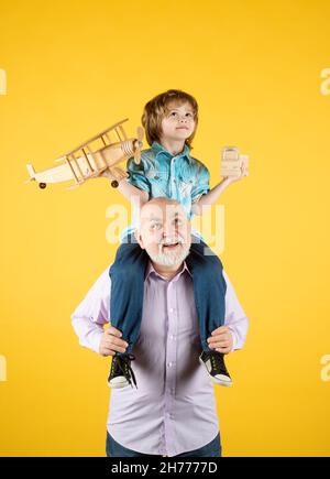 Großvater und Sohn Huckepack Fahrt mit Flugzeug und Holzspielzeug LKW. Männer Generation Großvater und Enkel. Ältere alte Verwandte mit Kind. Stockfoto