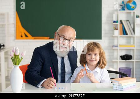 Oberlehrer oder Großvater und Schüler im Klassenzimmer der Schule. Privatunterricht. Der alte Lehrer hilft dem kleinen Schüler beim Lernen Stockfoto