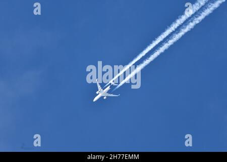 Ein weißes Flugzeug glitt über einen kristallklaren blauen Himmel mit zwei unterschiedlichen Dampfspuren, die am Himmel entlang hingen Stockfoto