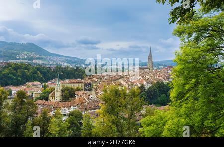Blick auf die mittelalterliche Stadt Bern, die Hauptstadt der Schweiz, mit einem Vordergrund von Bäumen und bewölktem Himmel im Hintergrund. Stockfoto