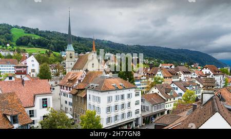 Panoramablick auf die Altstadt der Schweizer Stadt Zug mit grünen Hügeln im Hintergrund und bewölktem Himmel. Stockfoto