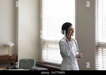 Lächelnde indische Ärztin, die im Büro telefoniert Stockfoto