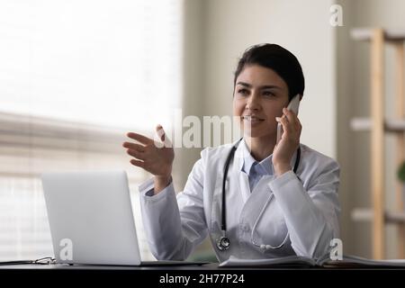 Lächelnde indische Ärztin, die am Telefon spricht und die Patientin konsultiert Stockfoto