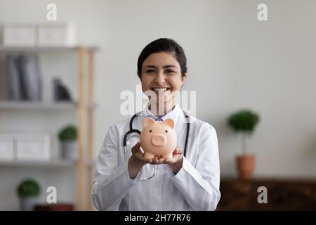 Kopf geschossen Porträt lächelnd indische Ärztin hält Sparschwein Stockfoto