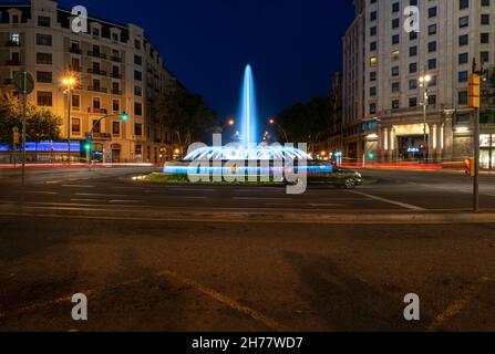 Der nächtliche Brunnen im Passeig de Gracia, einer der wichtigsten Straßen Barcelonas, ist beleuchtet. Ein Auto überquert die Kreuzung. Stockfoto