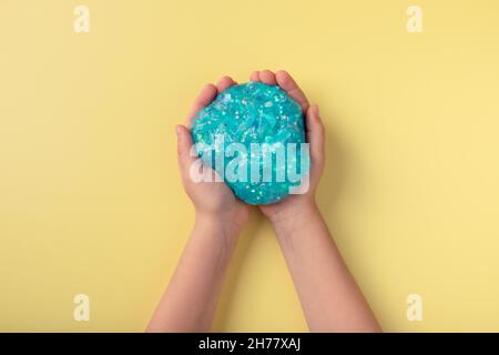 childs Hände mit blauem Glitzer Schleim über gelbem Hintergrund Stockfoto