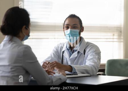 Lächelnder afroamerikanischer Arzt in medizinischer Maske, der indischen Patienten konsultiert Stockfoto