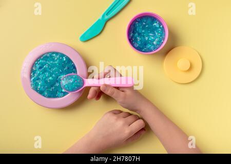 Mädchen spielt mit Spielzeug Küchenutensilien und blauen Glitzer Schleim Stockfoto