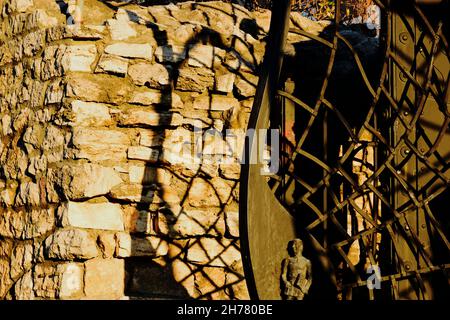 Dekorativ großes schwarzes schmiedeeisernes Tor mit starkem Schatten auf strukturierter rauer Steinwand. Architektonisches Detail aus der Nähe. Geschmiedeter Metallzaun. Stockfoto