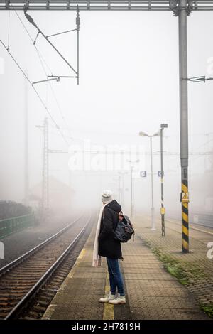 Alleinreisende Frau, die auf dem leeren nebligen Bahnhofsplatz auf den Zug wartet Stockfoto