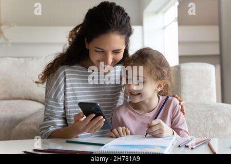 Glückliche Mutter mit Tochter abgelenkt vom Zeichnen mit dem Smartphone Stockfoto