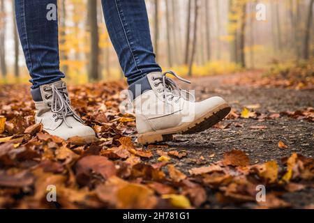 Wandern Sie mit Wanderschuhen auf der Straße im Herbstwald. Lederschuhe in gefallenen Blättern Stockfoto