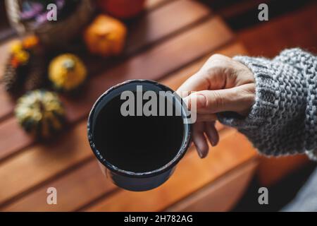Genießen Sie starken schwarzen Kaffee. Frau hält Tasse Heißgetränk in gemütlichen Innenraum mit Herbstdeko Stockfoto
