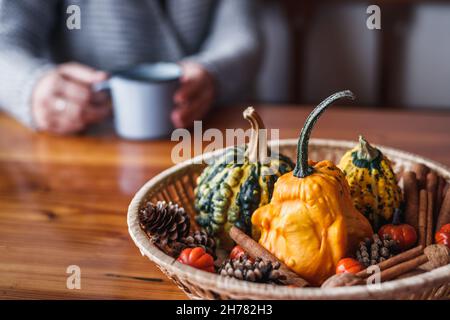 Herbstdekoration mit Kürbissen auf Holztisch. Unverschämtes Mädchen mit Strickpullover und heißem Kaffee Stockfoto